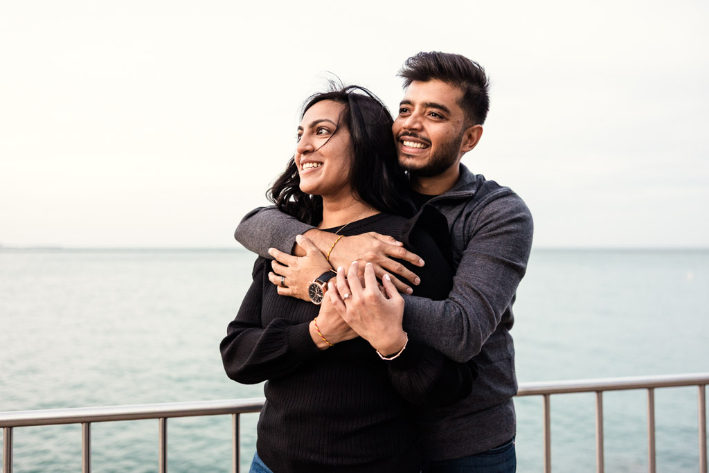 Smiling couple hugging by a waterfront railing near Lake Michigan during their Chicago fall engagement session