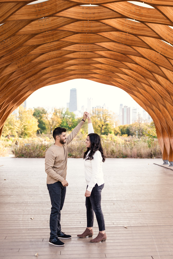 Engaged couple dances under the Lincoln Park Honeycomb with the Chicago skyline and autumn trees in the background