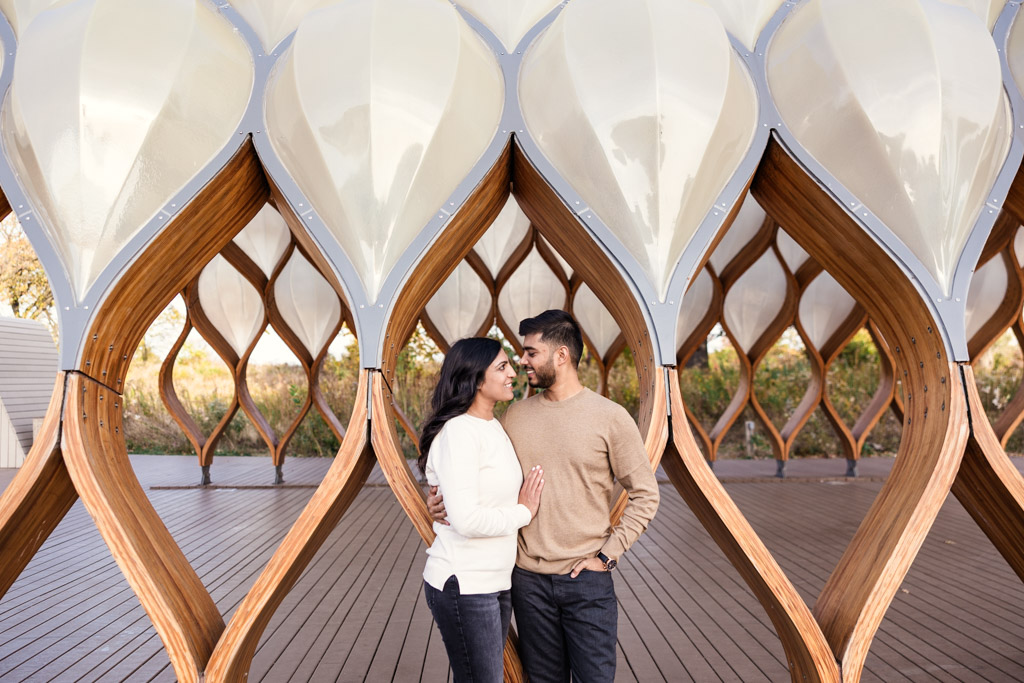 A couple stands close together, smiling, outside the Lincoln Park Honeycomb structure during their Chicago fall engagement session