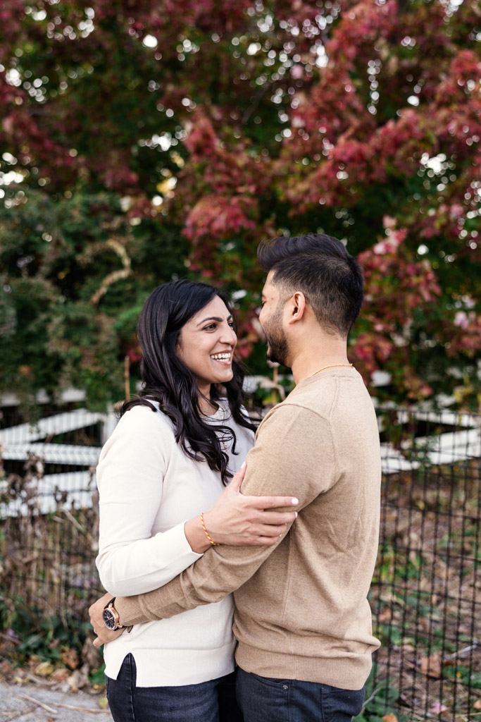 A couple smiles at each other, embracing outdoors in Lincoln Park with autumn leaves in the background during their Chicago fall engagement session