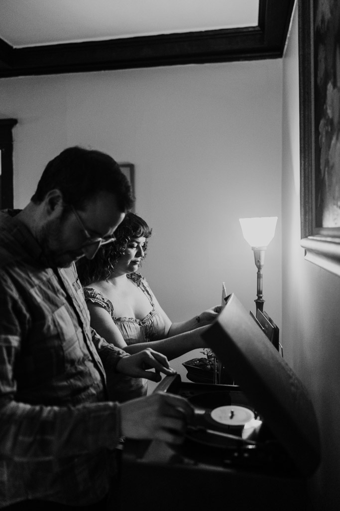 Black and white photo of man and woman selecting vinyl records by a record player in their softly lit Chicago home