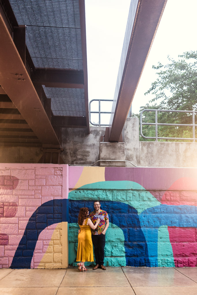 Couple stands together by a colorful mural under a large metal bridge during their Chicago engagement session in the Ravenswood neighborhood