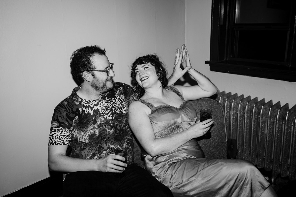Black and white photo of man and woman sitting on a couch in their Chicago home, smiling and holding drinks during their engagement session