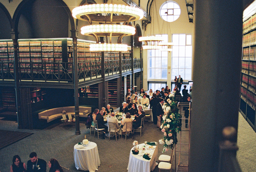 Film photo of guests seated at tables beneath balconies and chandeliers during The Library at 190 wedding reception