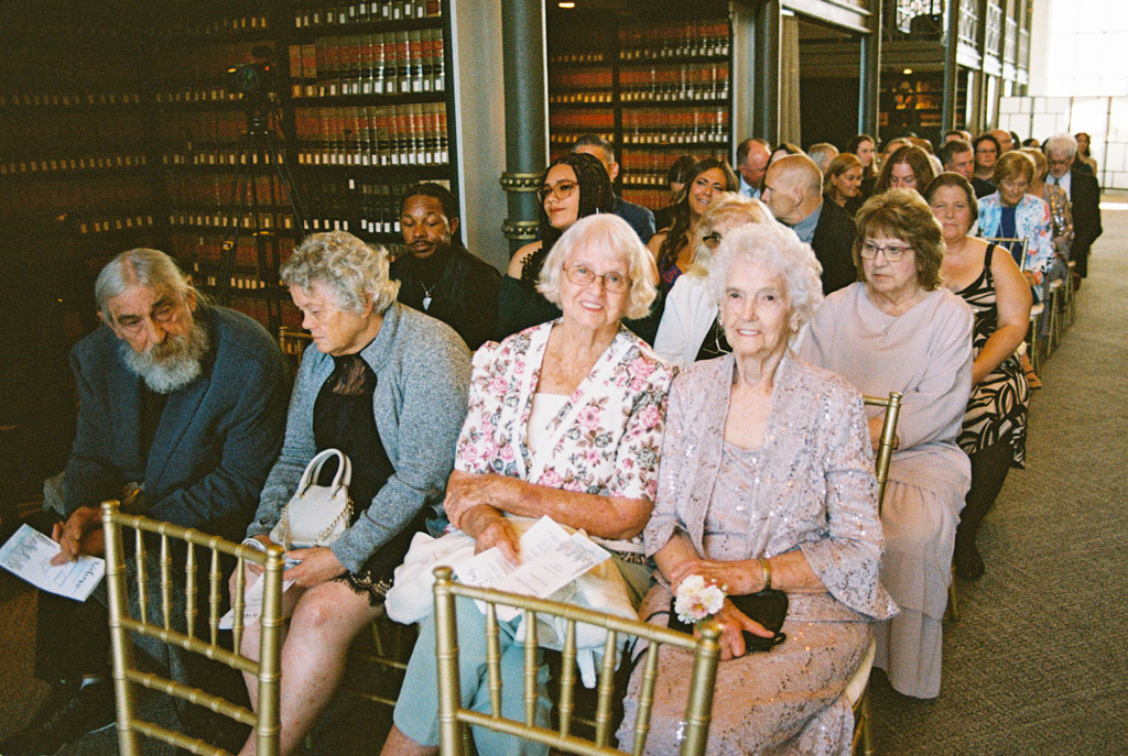 Film photo of guests seated in rows at a formal indoor event, smiling and waiting during wedding ceremony at The Library at 190 in downtown Chicago