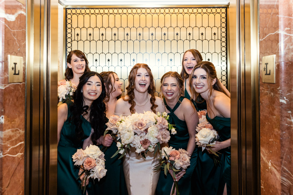 Bride and bridesmaids in green dresses holding bouquets inside a golden elevator before wedding ceremony at The Library at 190 in downtown Chicago