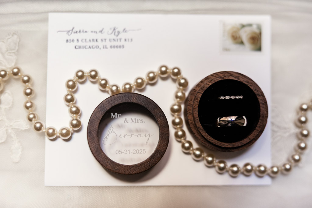 Wooden ring box containing two rings, a pearl necklace, and an envelope with wedding details are elegantly displayed on lace for wedding at The Library at 190 in downtown Chicago