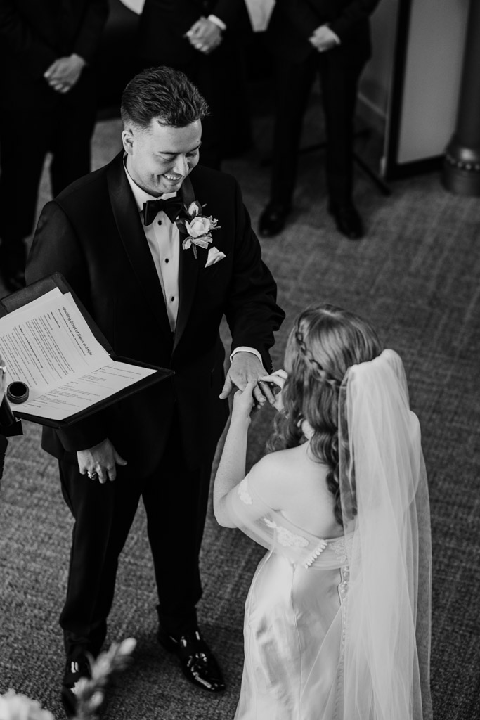 Black and white photo of bride putting ring on groom's hand during their wedding ceremony at The Library at 190 in downtown Chicago