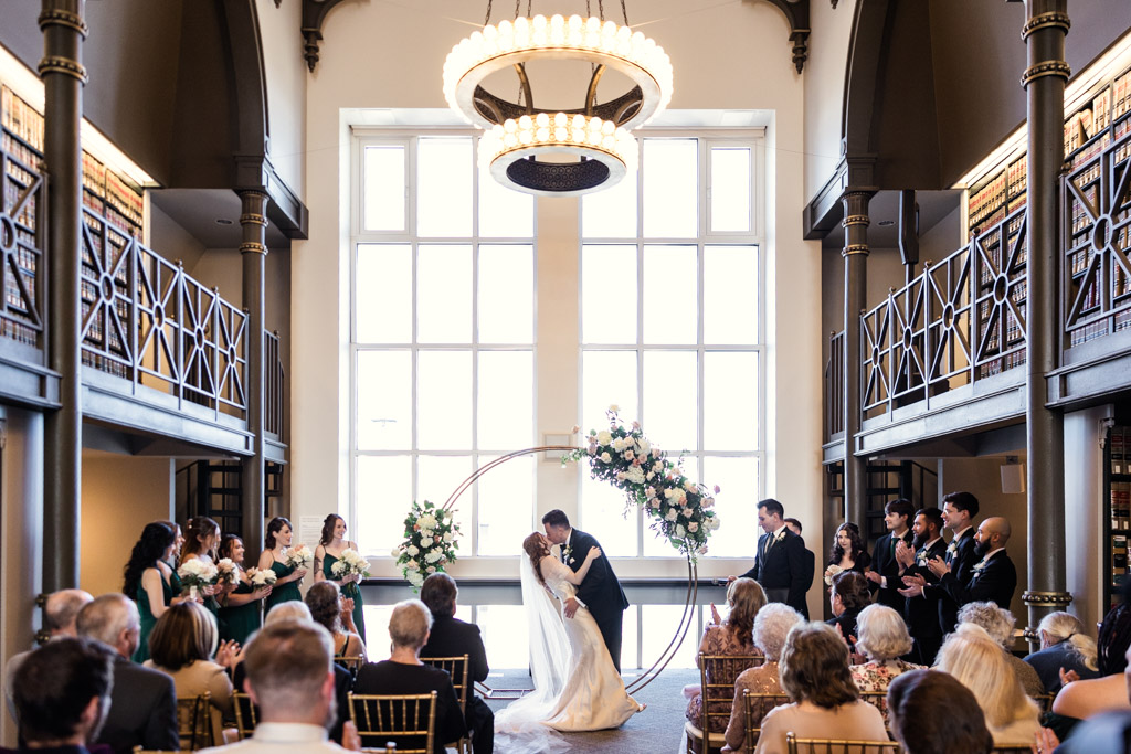 Bride and groom kiss during their downtown Chicago wedding at The Library at 190, surrounded by their wedding party and guests in a bright room