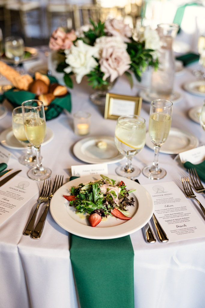 Fresh salad with strawberries graces a formal table set with menus, drinks, and a floral centerpiece for wedding reception at The Library at 190 in downtown Chicago