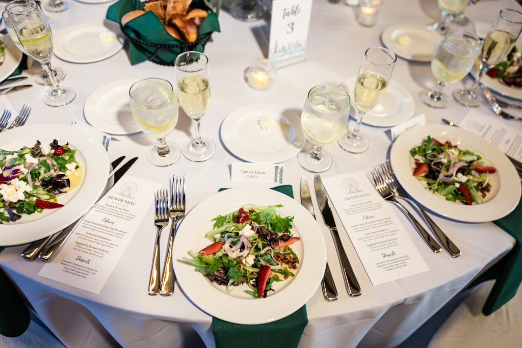 Guest table settings with plates of salad, menus, wine glasses, and water at Library at 190 wedding reception