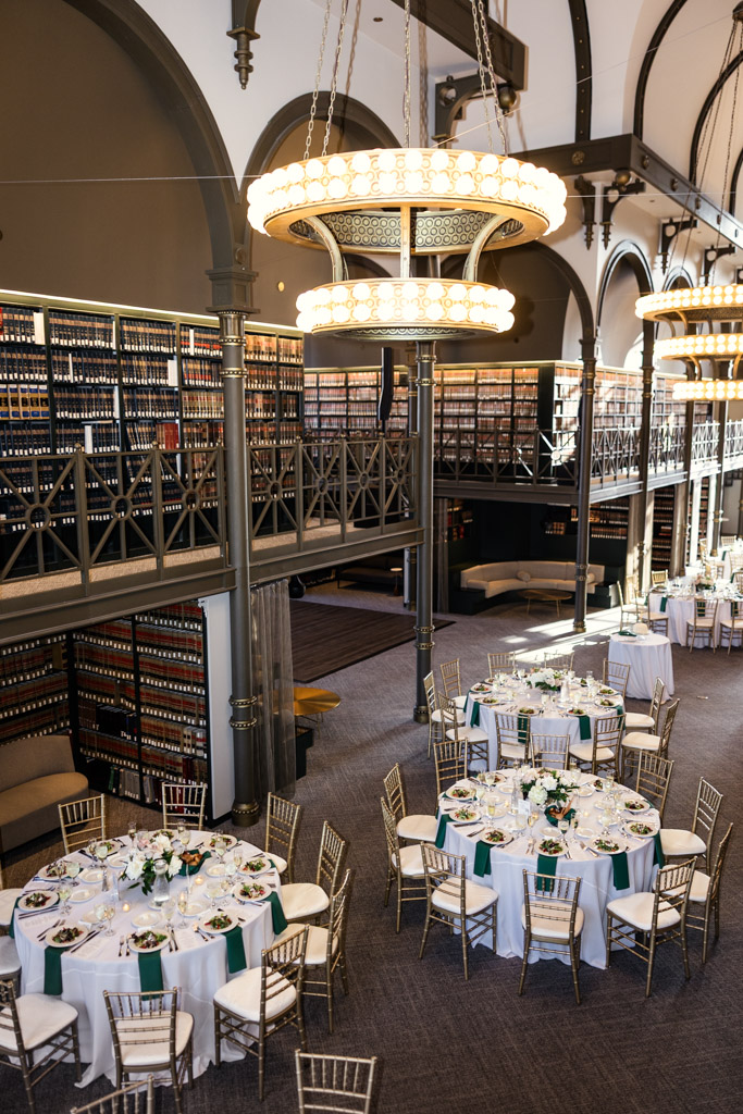 Wedding reception space with round tables, gold chairs, tall bookshelves and sparkling chandeliers at The Library at 190 in downtown Chicago
