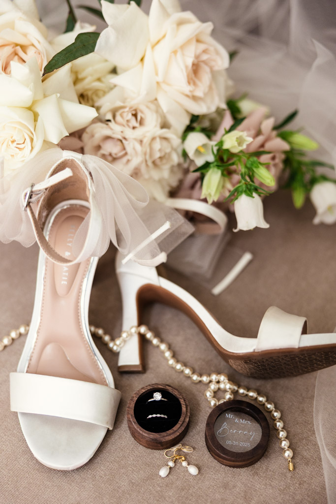 Bride's shoes, pearl jewelry, rings, and cream flowers arranged on a beige surface for The Library at 190 wedding