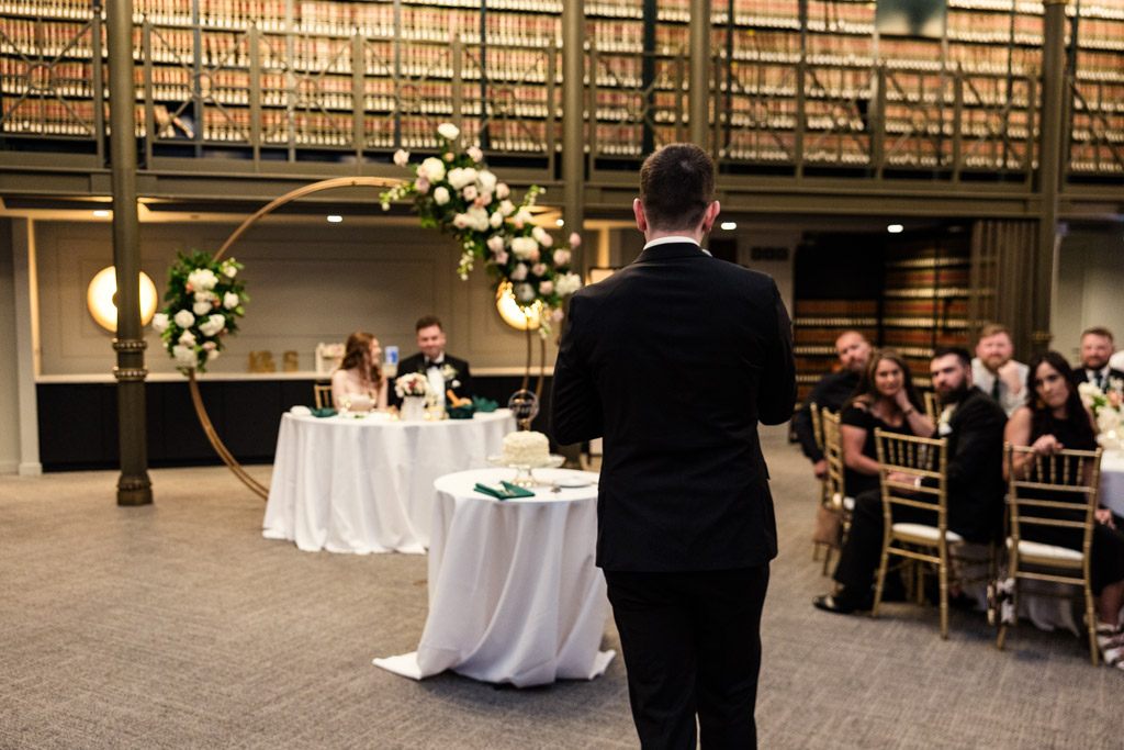 Officiant gives speech at Library at 190 wedding reception, with guests and newlyweds seated nearby