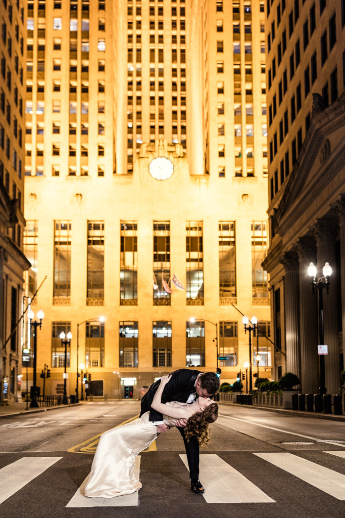Romantic photo of groom dipping and kissing bride on LaSalle Street in downtown Chicago at night, framed by tall, brightly lit buildings
