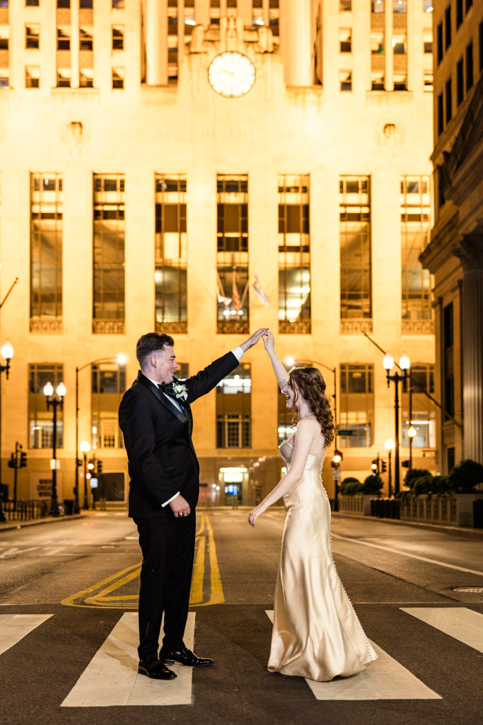 Bride and groom dance at night on LaSalle Street, illuminated by bright building lights behind them, outside The Library at 190 in downtown Chicago