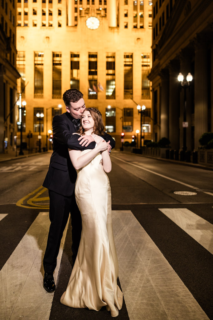 Bride and groom embrace and smile on LaSalle Street at night, illuminated by golden lights outside their The Library at 190 wedding reception