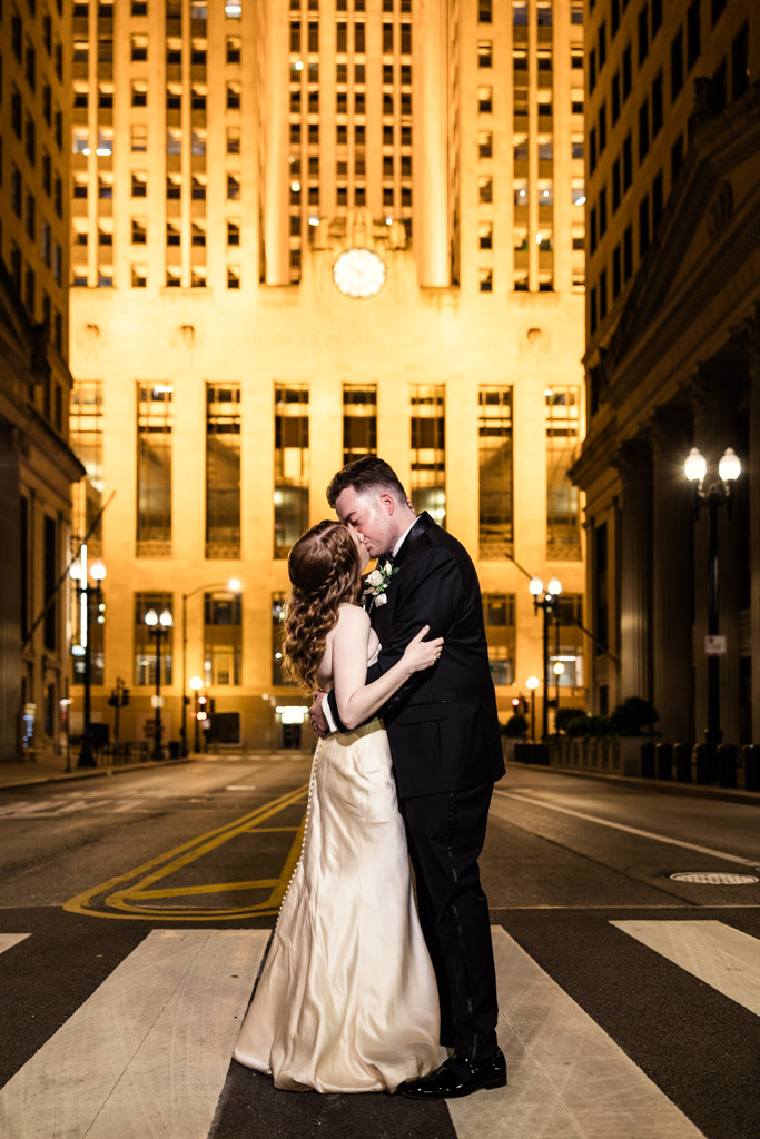 Bride and groom kiss in the middle of a city street at night, with the Chicago Board of Trade building behind them