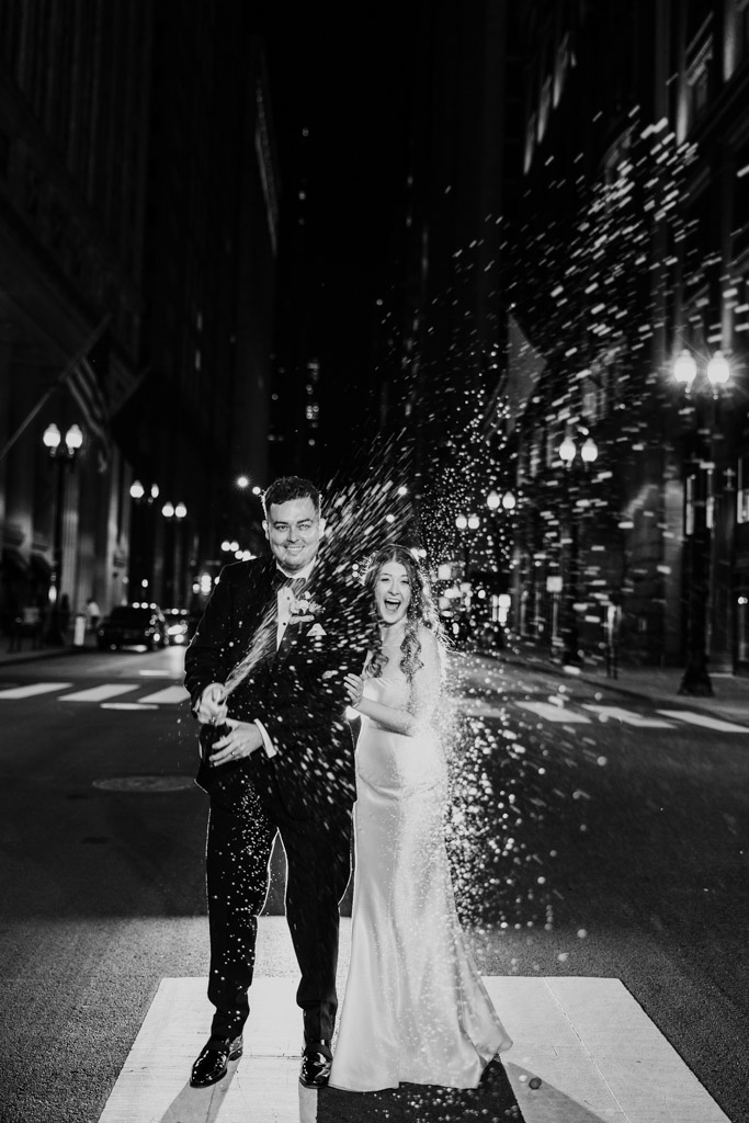Black and white photo of bride and groom popping champagne outside The Library at 190 in downtown Chicago