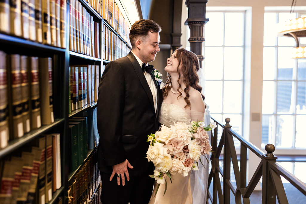 Bride and groom smile at each other, standing by bookshelves inside The Library at 190 in downtown Chicago