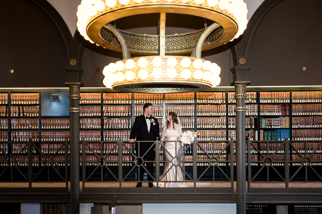 A bride and groom stand on a balcony under a large circular chandelier inside The Library at 190 in downtown Chicago