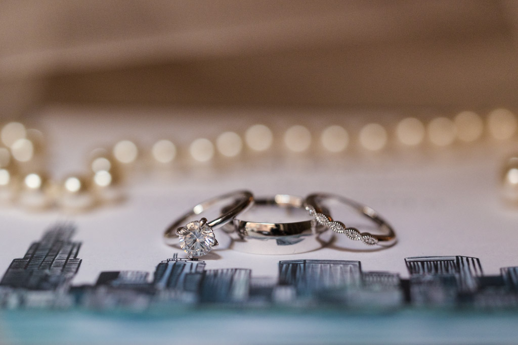 Detail photo of three rings, including a diamond engagement ring, rest beside a pearl necklace for wedding at The Library at 190 in downtown Chicago