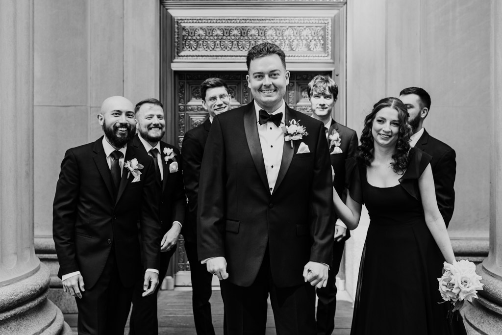 Black and white photo of groom and groomspeople in front of a golden door flanked by marble columns in downtown Chicago