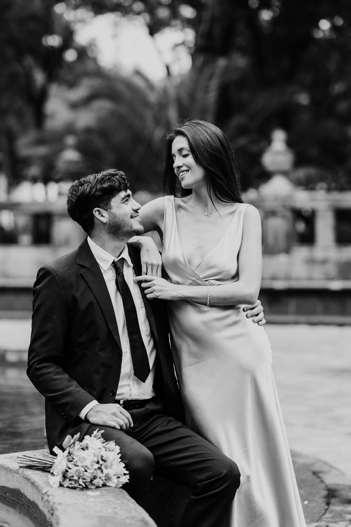 Newlywed couple dressed formally sits by a fountain in Alameda Central during their Mexico City elopement