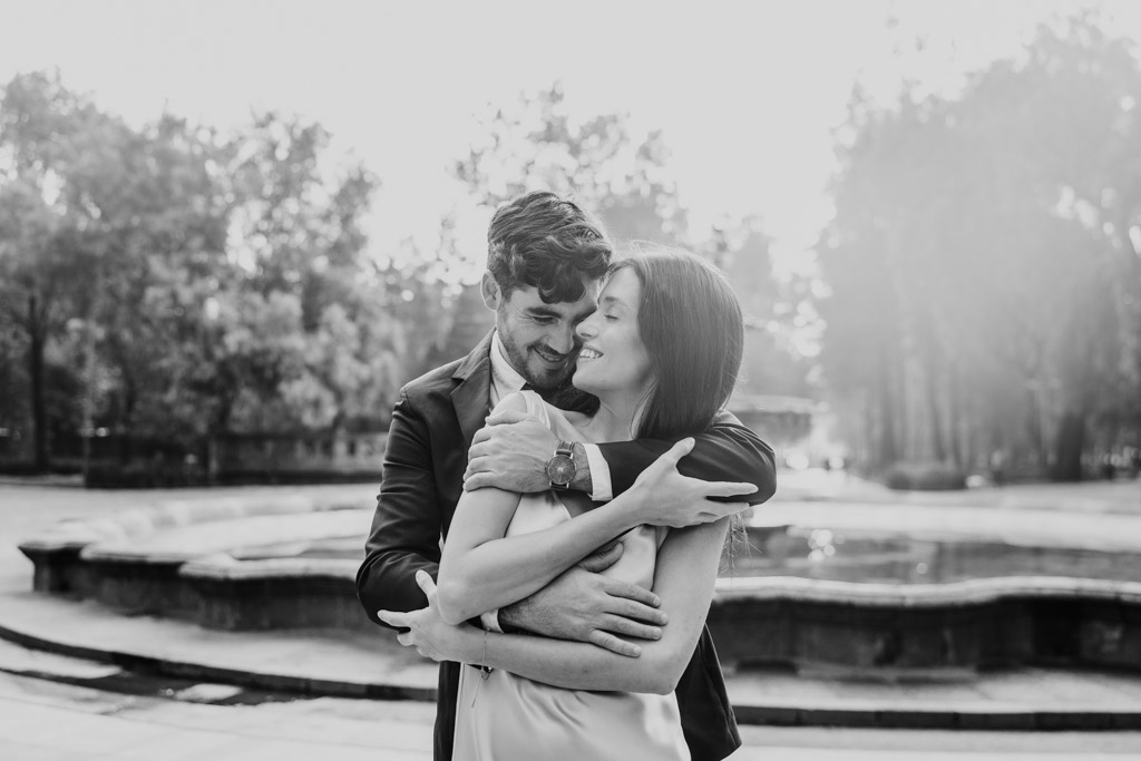Candid black and white photo of newlywed couple embraces and smiles near a fountain in Alameda Central during their Mexico City elopement