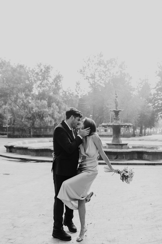 Black and white photo of couple embracing and kissing by a fountain in Alameda Central during their Mexico City elopement