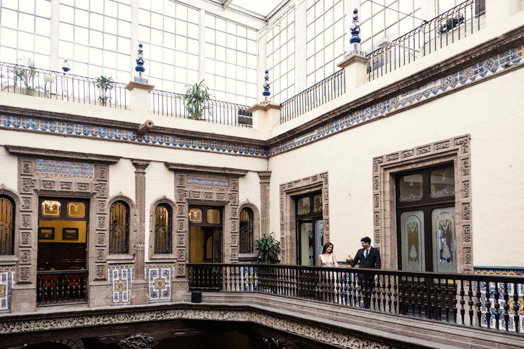 A couple stands on a balcony inside La Casa de los Azulejos with large windows and ornate details during Mexico City elopement