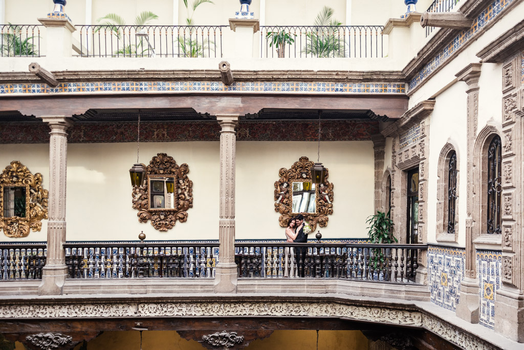 Couple in formal dress holds each other on a balcony in La Casa de los Azulejos during their Mexico City elopement