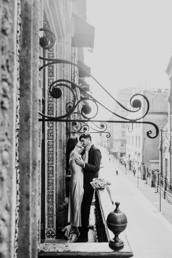 Black and white photo of couple holding each other on a balcony at La Casa de los Azulejos above a quiet city street during their Mexico City elopement