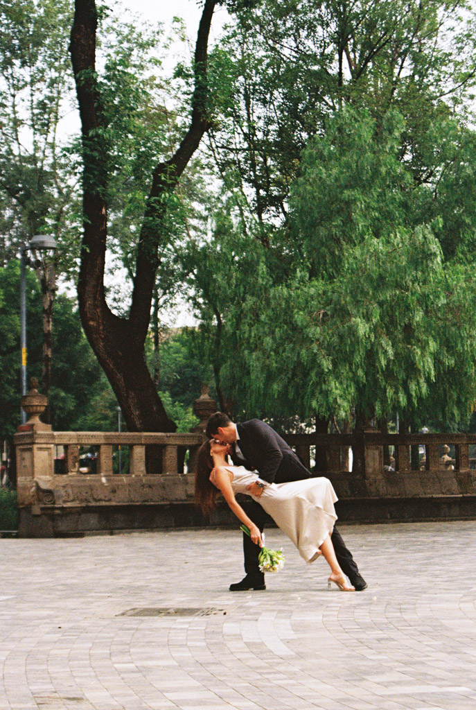 Romantic film photo of man dipping his partner on a stone plaza in Alameda Central, surrounded by green trees during their Mexico City elopement