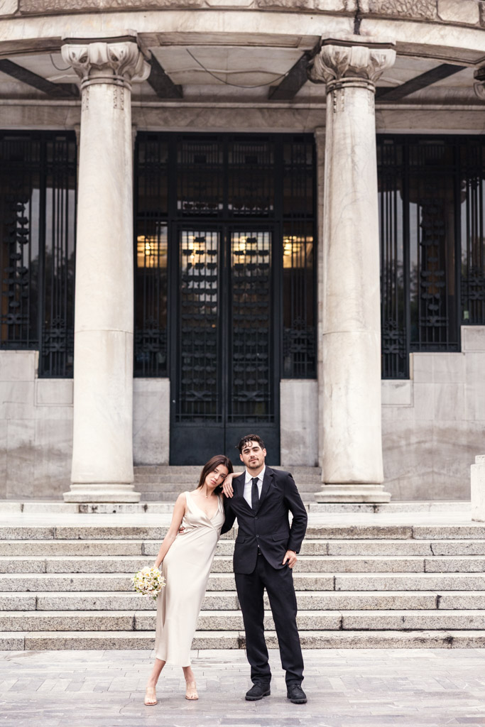A couple in formal attire stands in front of stone steps at Palacio de Bellas Artes during their Mexico City elopement session