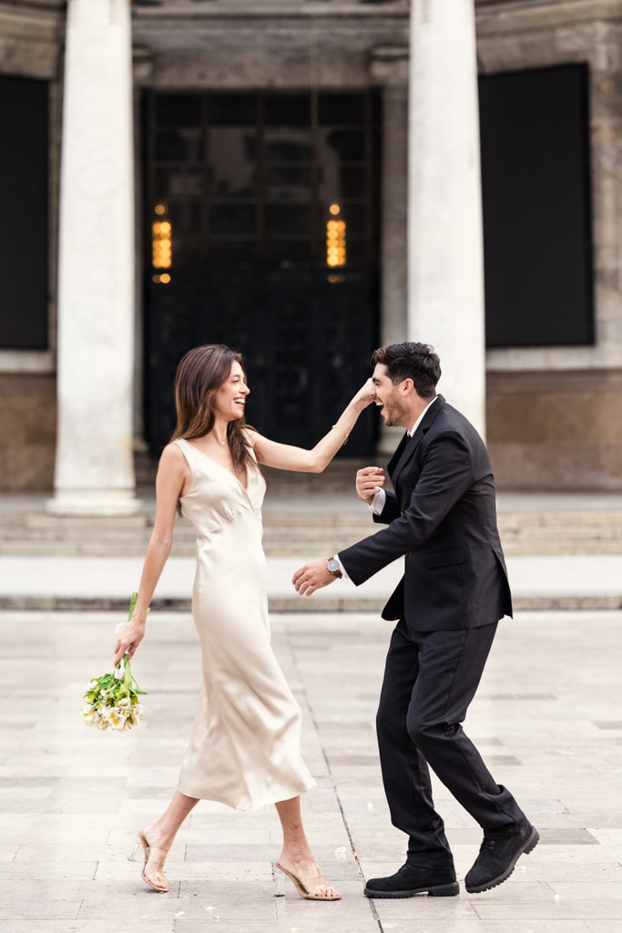Happy newlywed couple, dressed formally, playfully interacts outside Palacio de Bellas Artes during their Mexico City elopement; the woman holds a bouquet