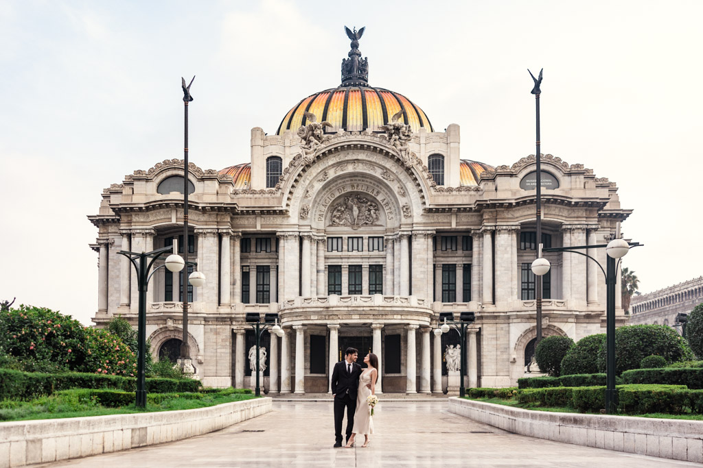 A couple stands in front of the ornate Palacio de Bellas Artes during their Mexico City elopement on a clear day