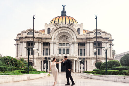 Groom kisses his partner's hand as they walk in front of the Palacio de Bellas Artes during their Mexico City elopement