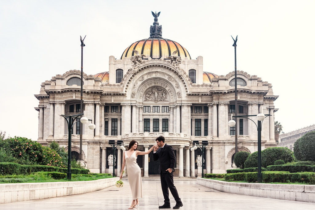 Groom kisses his partner's hand as they walk in front of the Palacio de Bellas Artes during their Mexico City elopement