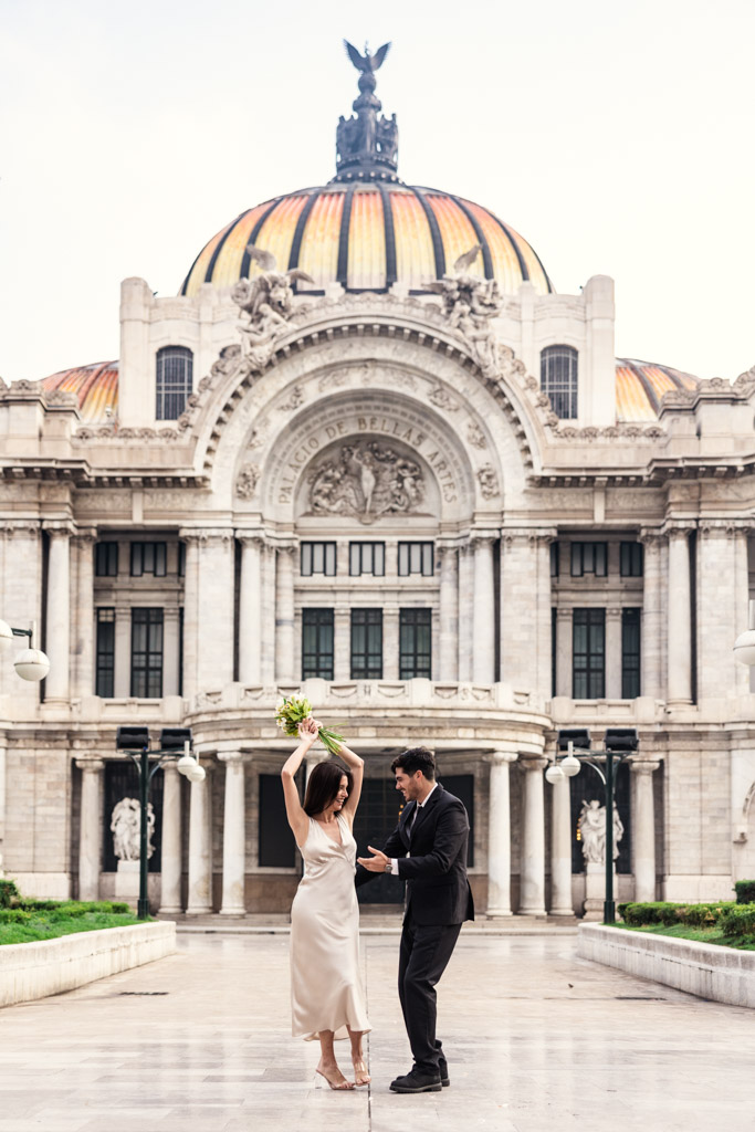 A couple in formal attire dances in front of the Palacio de Bellas Artes domed roof during their Mexico City elopement