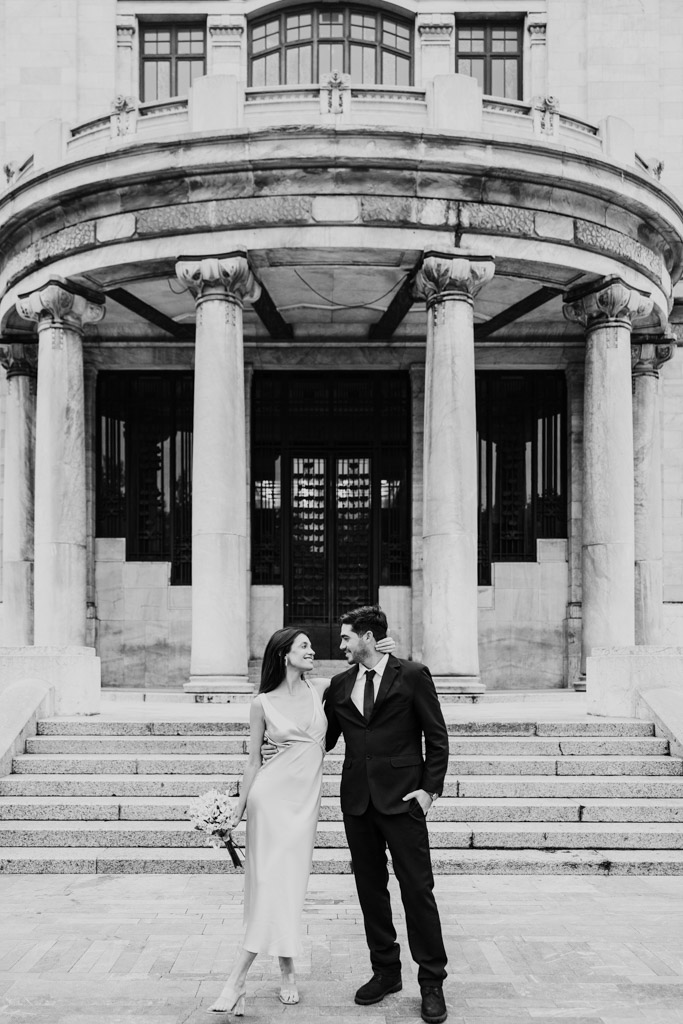 Black adn white photo of newlyweds dressed formally standing smiling at each other in front of Palacio de Bellas Artes their Mexico City elopement