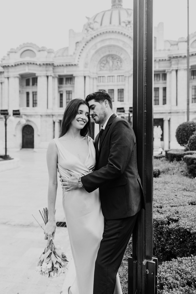 Black and white photo of newlywed couple in formal attire in front Palacio de Bellas Artes during Mexico City elopement