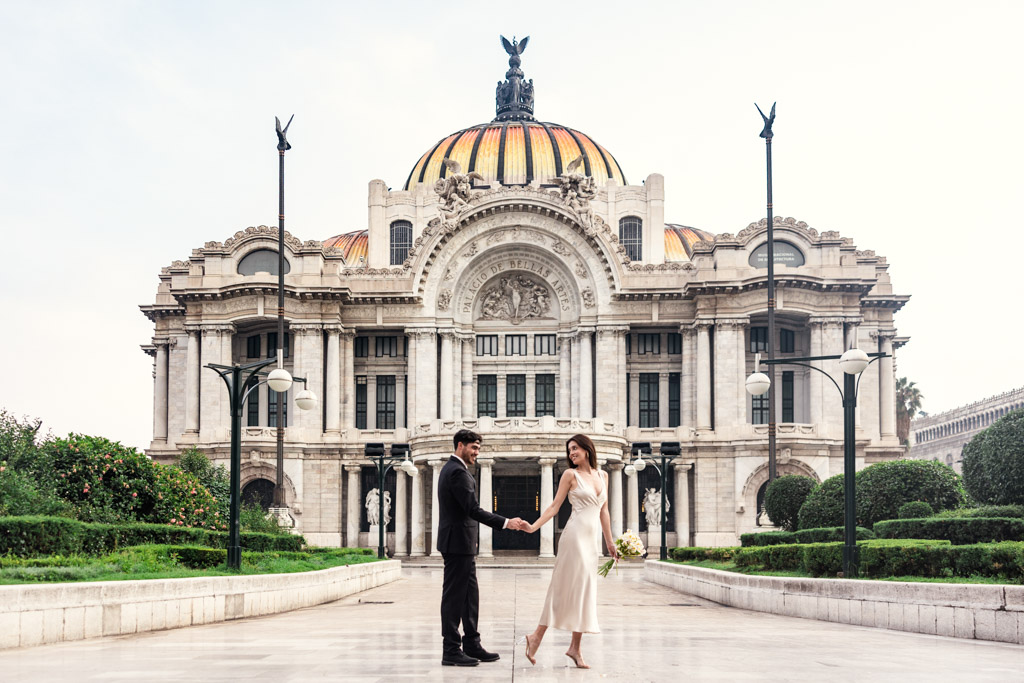 A couple holds hands in front of the Palacio de Bellas Artes during their Mexico City elopement on a clear day