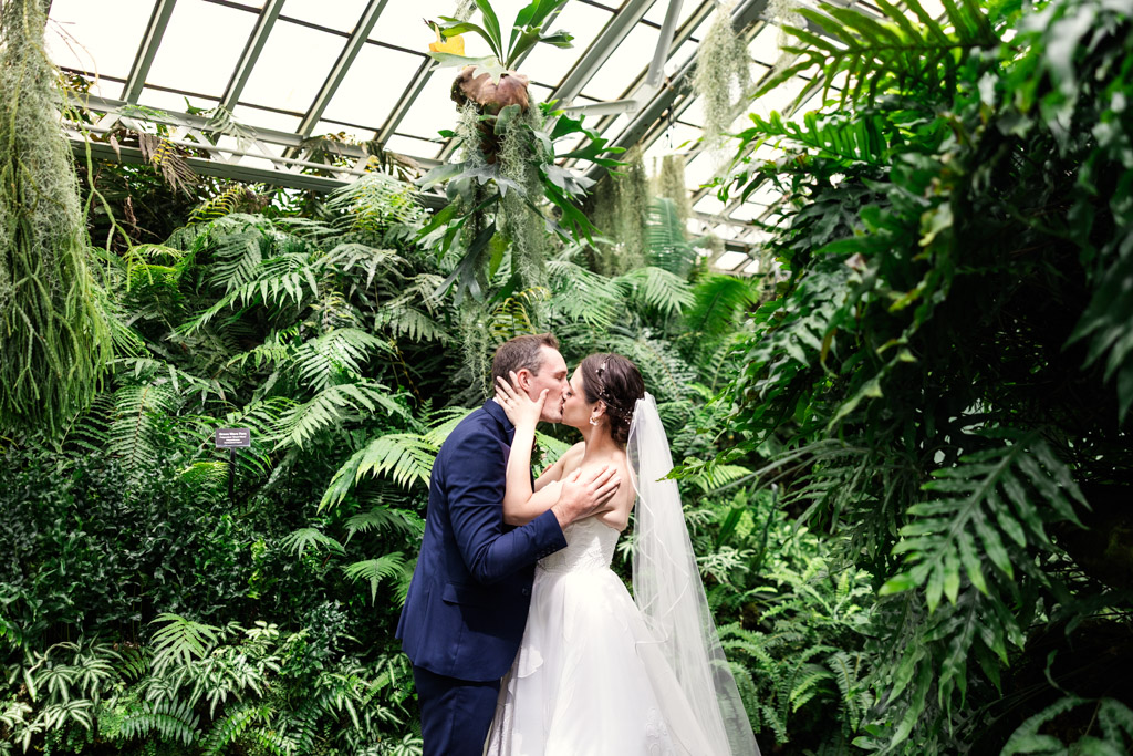 Bride and groom kiss surrounded by lush greenery in the Fern Room at Garfield Park Conservatory