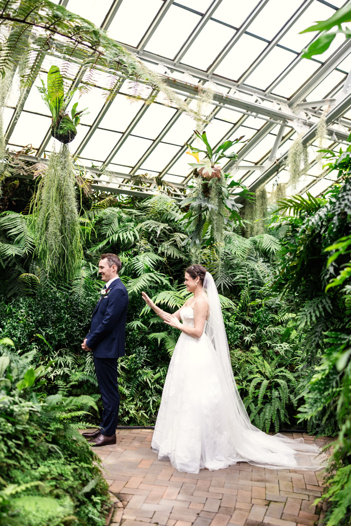 Bride approaches groom from behind in during their first look in the Fern Room of the Garfield Park Conservatory