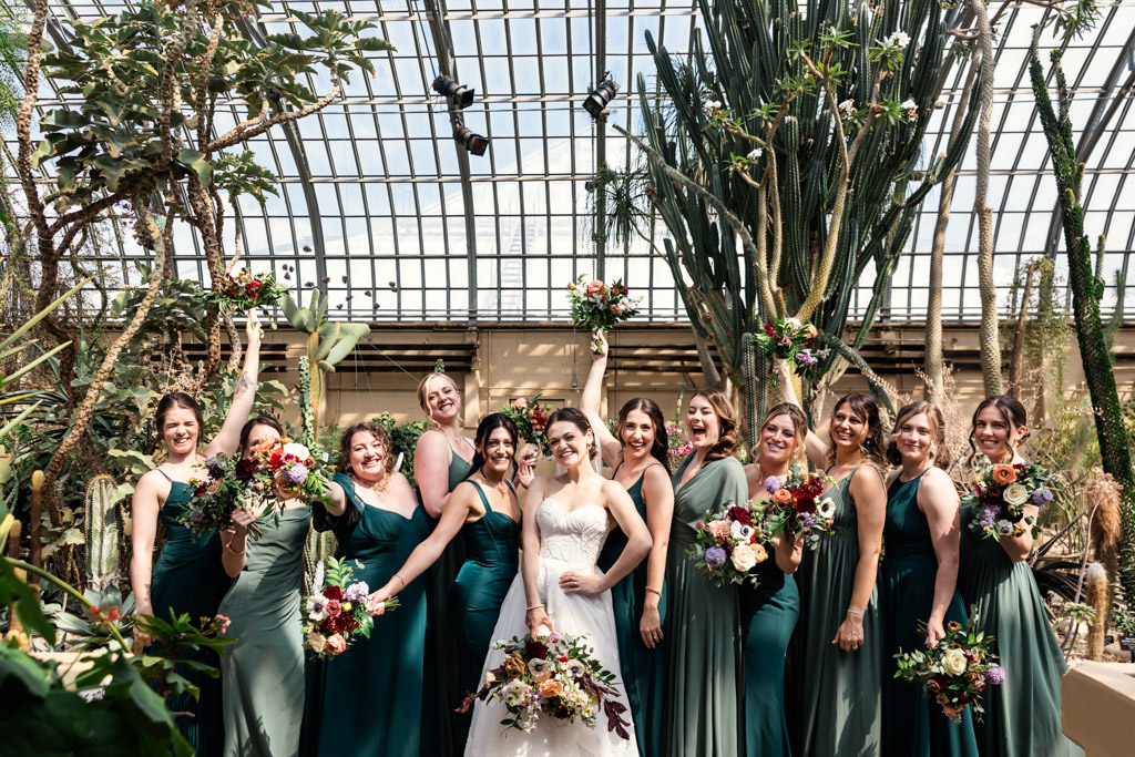 Portrait of bride in whiteand bridesmaids in green dresses, all holding bouquets, inside Garfield Park Conservatory's Desert Room