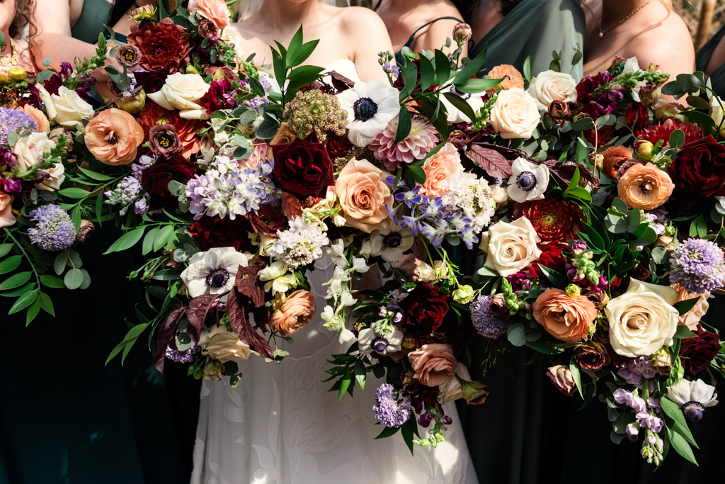 Bride and bridesmaids hold their colorful bouquets of assorted flowers together while at Garfield Park Conservatory