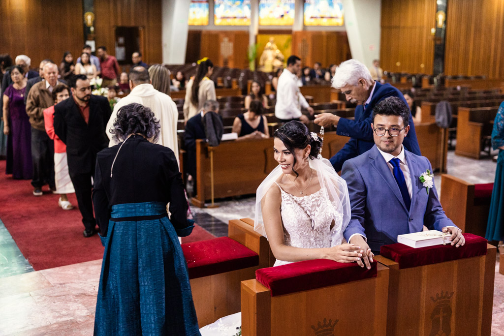 Bride and groom kneel while guests begin El Lazo ceremony during Parroquia San Cayetano wedding