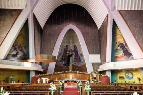 Interior of Parroquia San Cayetano with decorated altar, pews, large arch, and religious murals