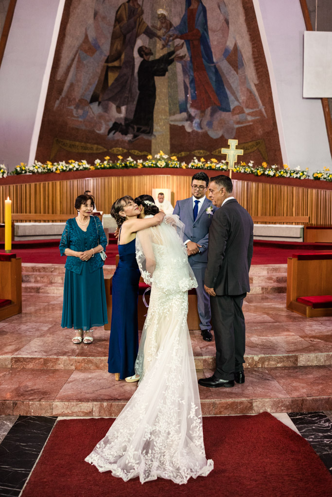 A bride in a white dress hugs a her mother at the altar of Parroquia San Cayetano during wedding ceremony